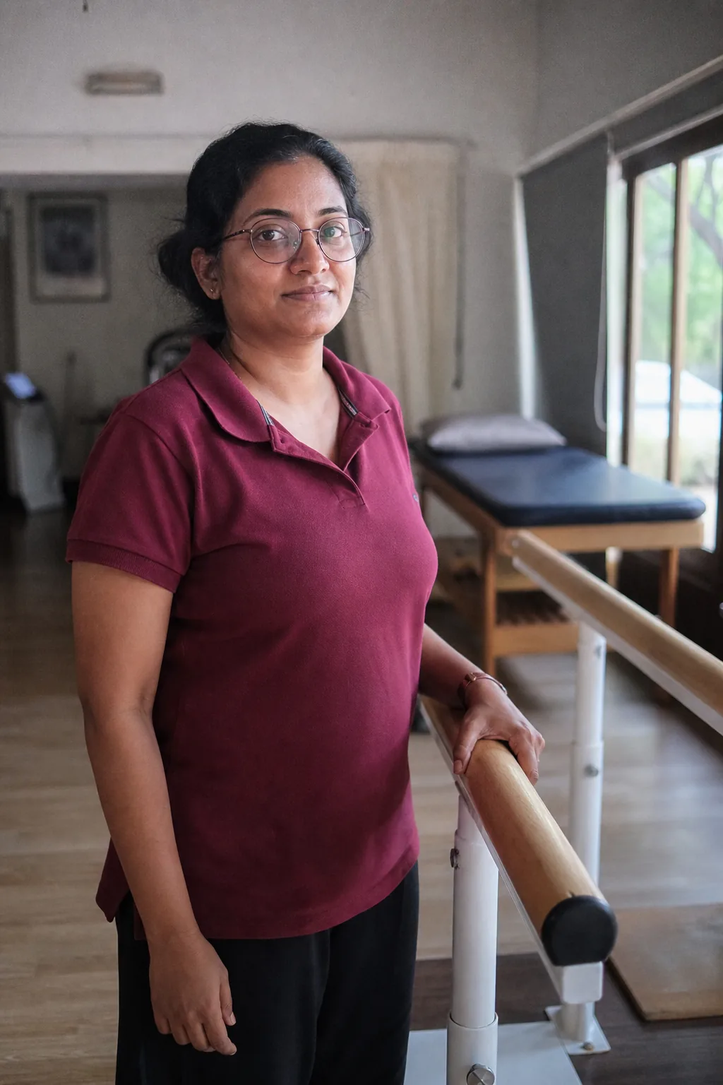 Deepa Gowda standing at the end of the parallel bars in the clinic.