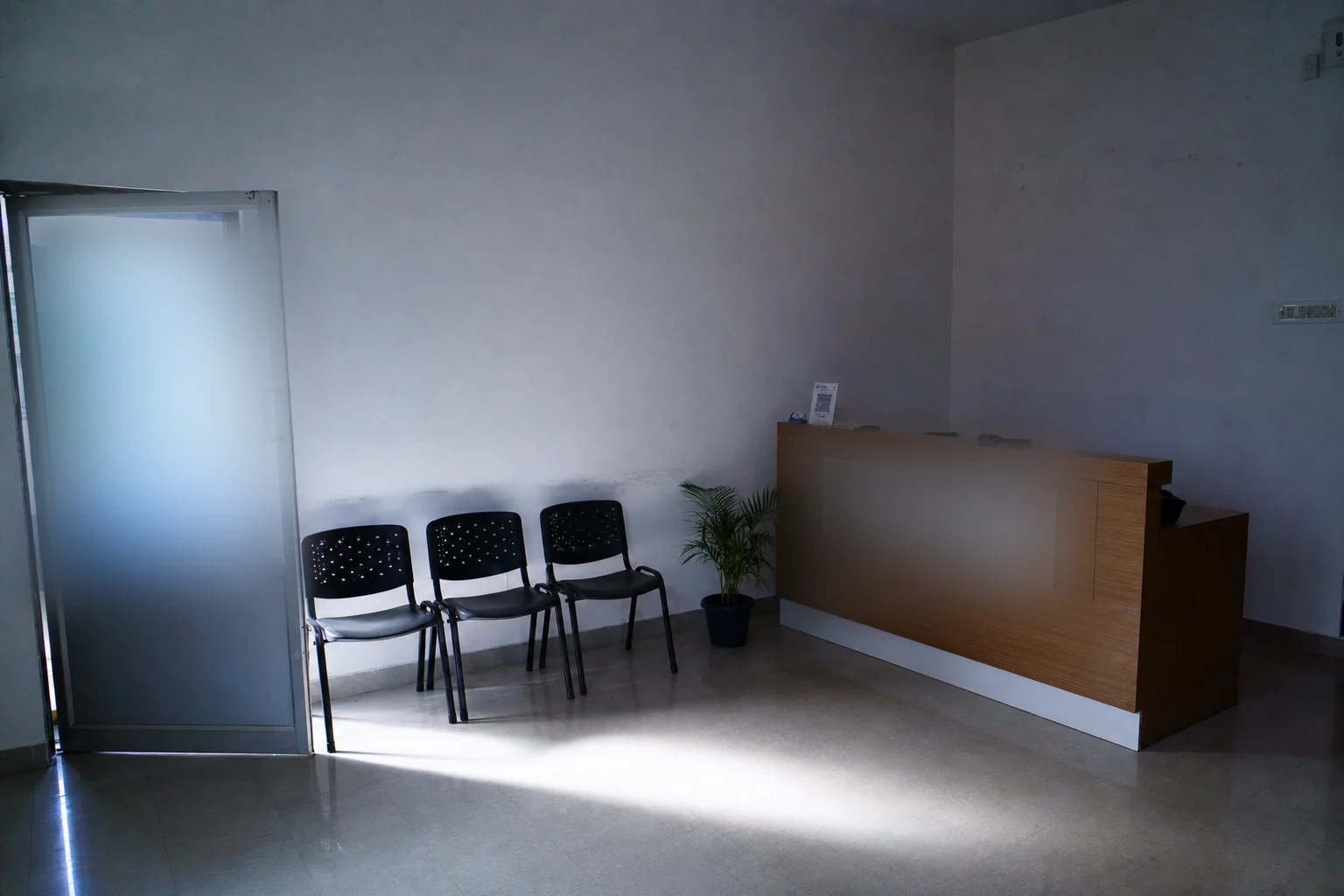 The empty reception of the clinic in the morning, with light from the open glass door falling across the tiled floor.