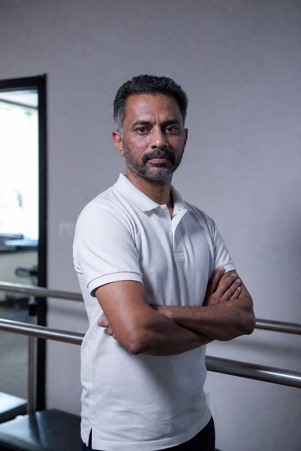 Dr Aravind Kandula standing with his arms folded beside the parallel bars in his Hyderabad clinic, looking at the camera.